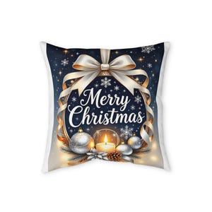 Op de afbeelding: Een vierkant sierkussen met een donkerblauwe achtergrond en de tekst Merry Christmas in wit schrift. Het ontwerp bevat een grote witte strik, zilveren ornamenten, een brandende kaars en witte sneeuwvlokken op een sterrenhemel.