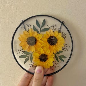 Op de afbeelding: Set van drie keramische mokken met een gespikkelde, cr&egrave;mekleurige glazuur. Elke mok heeft een handgeschilderd bloemmotief in blauw, groen en geel. De mokken hebben een eenvoudige, afgeronde vorm en een handvat.