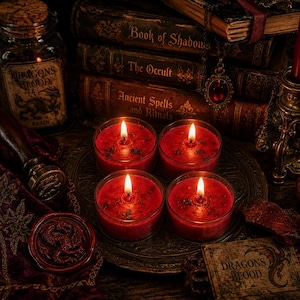 May include: Four red candles in clear glass votives are lit, casting a warm glow. They are arranged on a dark metal tray surrounded by antique books titled Book of Shadows, The Occult, and Ancient Spells and Rituals, plus a jar of Dragons Blood.