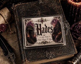 May include: A rectangular clear plastic container of soy wax melts featuring a label with the text Hades, soy wax, and Pink Petals N Lace. The label displays an illustration of a dark stone archway, a crescent moon, and a small boat on water.