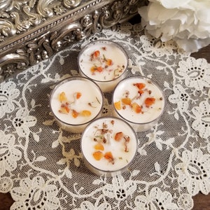 May include: Four white tea light candles with orange and white crystals embedded in the wax. The candles are on a white lace doily.