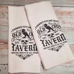 May include: Two white kitchen towels with a black graphic design. The design features a skull, a crow, and the text "Old Crow Tavern Est. 1963. Strongest Ales and Tales. Serving Spirits of All Kinds."