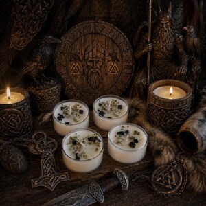 May include: Four small white candles in clear containers, topped with dark stones and dried herbs. The candles are arranged among Norse-themed items, including a circular wooden plaque with a bearded figure, a metal hammer pendant, and a dagger.