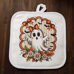 May include: White square pot holder with a cute ghost design. The ghost has a bow and is surrounded by orange bows, bats, and fall foliage. The pot holder has a white loop for hanging.