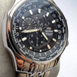 May include: A silver Orient men's wristwatch with a black face and a world time dial. The watch has a silver band and a date window at the 3 o'clock position. The watch face features the text "Orient Automatic Sapphire".