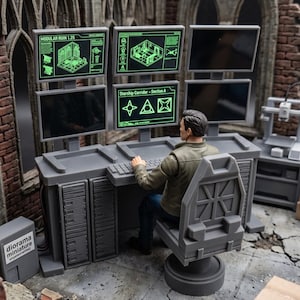 May include: A miniature gray computer workstation with five monitors, a keyboard, and a swivel chair. Two monitors display green technical diagrams with text reading Modular Ruin 1.25 and Starship Corridor - Section A. A small box is labeled diorama miniature.