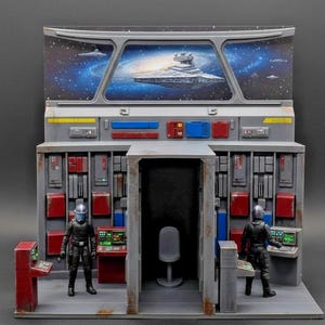 May include: A detailed diorama of a spaceship interior, featuring two figures in black uniforms and helmets. The scene includes control panels, a chair, and a window displaying a galaxy with a large starship. The color scheme is primarily gray, red, and blue.