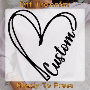 May include: A white t-shirt with a black heart design and the word "Custom" written inside the heart. The text "Dtf Transfer" is at the top of the image and "Ready To Press" is at the bottom.