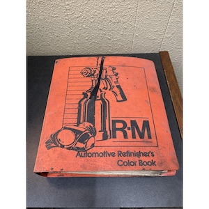 May include: An orange Automotive Refinisher's Color Book with black illustrations of spray guns and paint bottles. The book has the letters "R-M" in large, bold letters. The title "Automotive Refinisher's Color Book" is printed at the bottom.