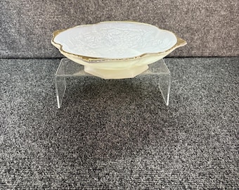 May include: A shallow, off-white milk glass bowl with an iridescent finish and a scalloped edge trimmed in gold. The interior features a molded relief pattern of grapes and leaves, resting on a small pedestal base.