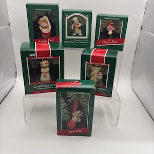 May include: A collection of six Hallmark Keepsake Christmas ornament boxes featuring various animal characters. The boxes are green with red accents and display images of a kitten in a stocking, a polar bear, a mouse, a cat, a bear, and a mouse on a spoon.