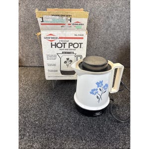 May include: Vintage West Bend Hot Pot, a 2 to 5 cup electric water heater and server. The white pot features blue floral designs and a black lid. The original box is included, with the text "HEAT AND SERVER".