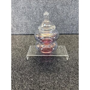 Op de afbeelding: Een heldere glazen pot met een deksel, gestapeld in twee secties, met een roze en goud iriserende glans. De pot staat op een heldere acryl displaystandaard. De achtergrond is een grijs tapijt.