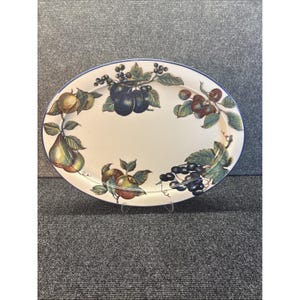 May include: Oval serving platter with a white background and a blue rim. The platter is decorated with colorful illustrations of various fruits, including pears, plums, and grapes. A decorative piece for serving food.