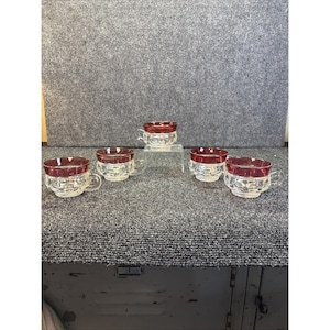 Peut inclure: Cinq tasses à thé en verre transparent avec un bord et une anse rouge rubis. Les tasses ont un motif décoratif à l'extérieur. Les tasses à thé sont disposées sur une surface grise.