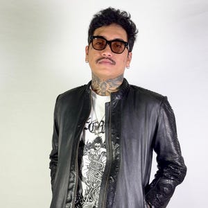 May include: Black leather jacket with snake-skin textured detailing on the shoulders and trim. The jacket features a zip closure and a stand-up collar. A white t-shirt with a graphic print is visible. The text "AKARYO" is printed on the shirt.