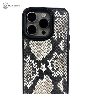 Pode incluir: Uma capa de telefone de pele de cobra branca e preta com uma protuberância de câmera preta e quatro lentes.