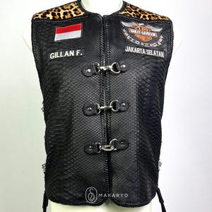 May include: Black leather vest with a snakeskin texture, leopard print collar. Patches include the Indonesian flag, "GILLAN F.", and a Harley-Davidson logo with "JAKARTA SELATAN". The vest has metal clasps and decorative chains.
