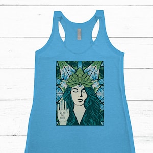 May include: Light blue tank top with a graphic of a woman with long teal hair, a green crown, and a third eye. The woman is holding up her hand with the words "READ THE BOOK" printed on it.