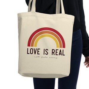 May include: A beige tote bag with a rainbow design and the text "LOVE IS REAL not fade away".