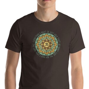 May include: A brown t-shirt with a green and gold mandala design featuring the Om symbol and the text "Everything's right so just hold tight - the long night's over and the sun's coming up."
