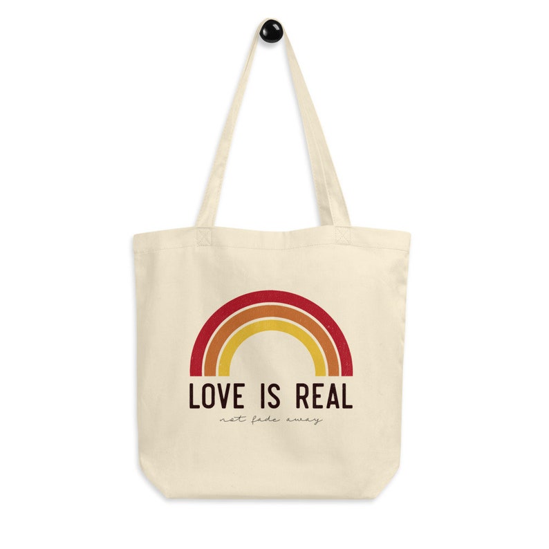 May include: A beige canvas tote bag with a rainbow design and the text "LOVE IS REAL not fade away".
