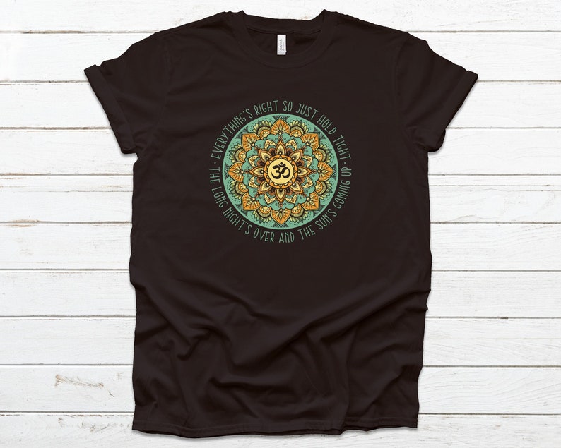 May include: Black t-shirt with a green and gold mandala design and the text "Everything's right so just hold tight - the long night's over and the sun's coming up."