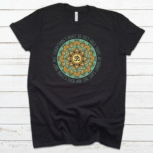 May include: Black t-shirt with a green and yellow mandala design featuring the Om symbol and the text "Everything's right so just hold tight - the long night's over and the sun's coming up."