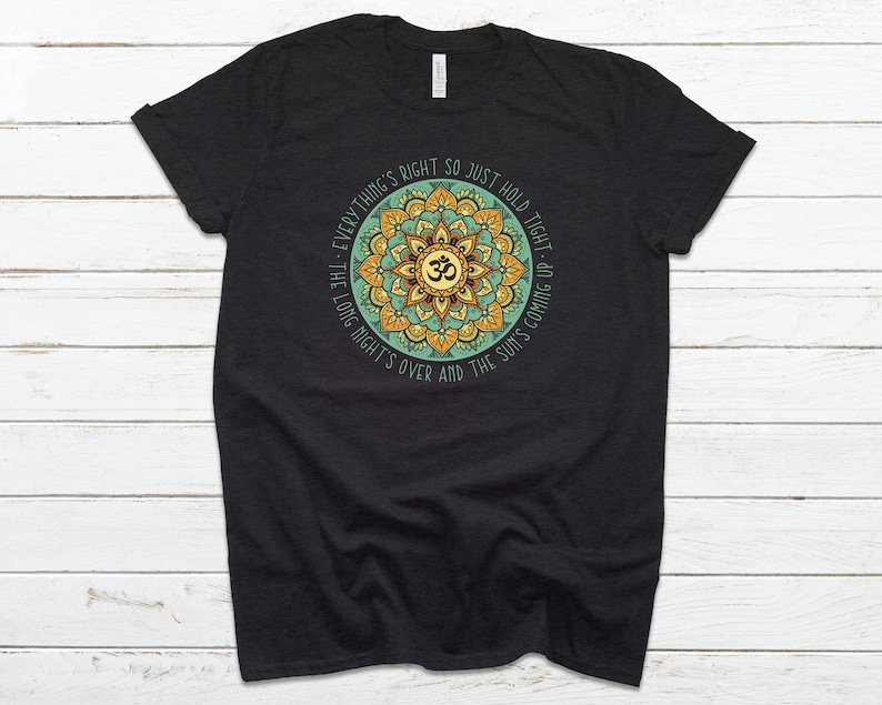 May include: Black t-shirt with a green and yellow mandala design featuring the Om symbol and the text "Everything's right so just hold tight - the long night's over and the sun's coming up."