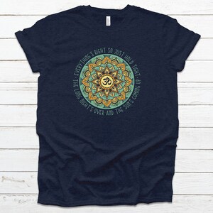 May include: Navy blue t-shirt with a mandala design featuring the Om symbol and the text "Everything's right so just hold tight - the long night's over and the sun's coming up."