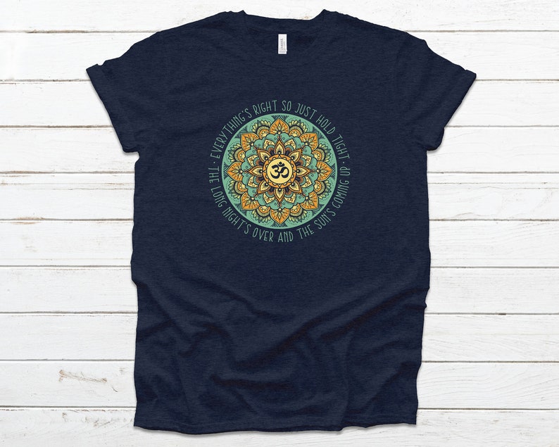 May include: Navy blue t-shirt with a mandala design featuring the Om symbol and the text "Everything's right so just hold tight - the long night's over and the sun's coming up."