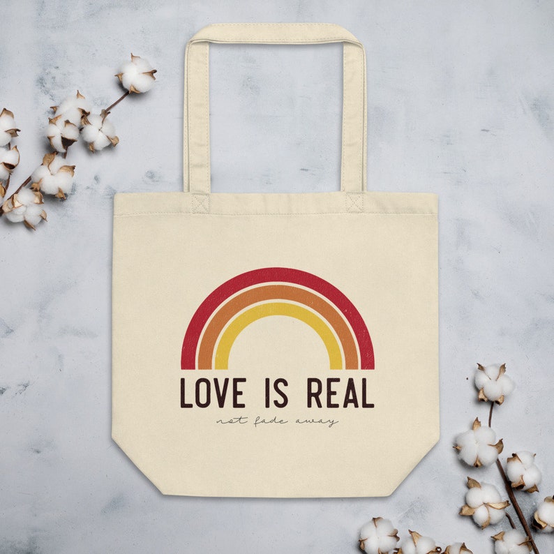 May include: A beige tote bag with a rainbow design and the text "LOVE IS REAL not fade away".