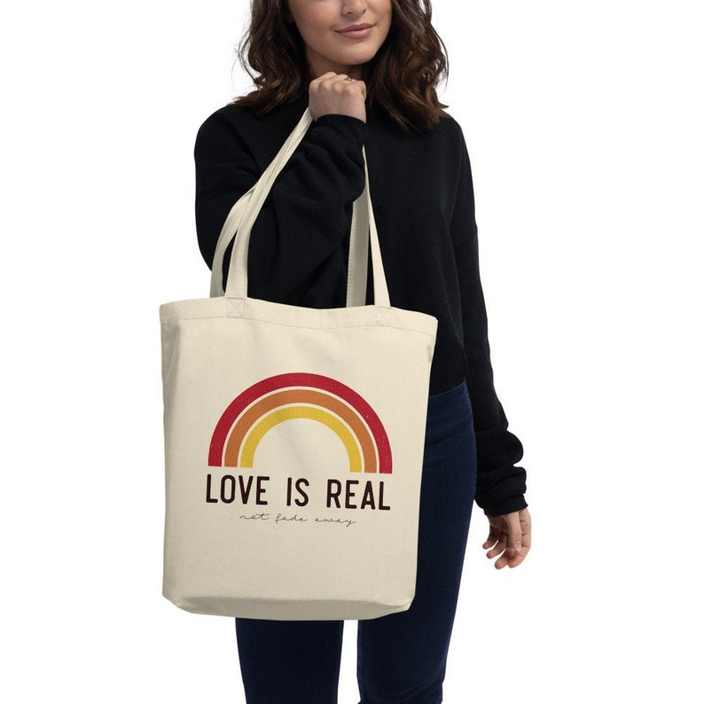 May include: A beige tote bag with a rainbow design and the text "LOVE IS REAL not fade away".