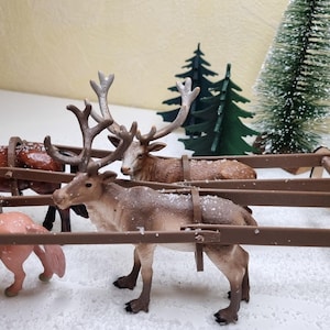 Könnte beinhalten: Eine Miniatur-Weihnachtsszene mit einem Holzschlitten, der von zwei Pferden und zwei Rentieren gezogen wird. Die Pferde sind braun und rosa, während die Rentiere große Geweihe haben. Miniatur-Weihnachtsbäume im Hintergrund schaffen eine festliche Atmosphäre.
