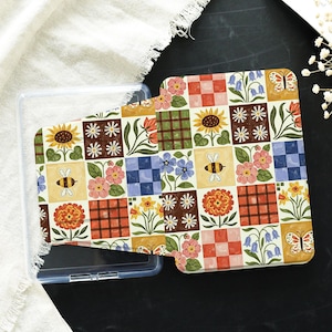 Op de afbeelding: Een decoratieve telefoonhoes met een kleurrijk patchwork-ontwerp met zonnebloemen, bijen, bloemen en vlinders. De hoes zit in een doorzichtige plastic hoes.