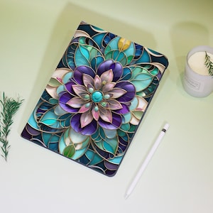 Peut inclure: Une coque de tablette avec un motif floral en vitrail dans les tons de violet, turquoise et or. L'étui présente une fleur centrale avec un centre turquoise et est entouré de formes détaillées en forme de feuilles. Un stylet blanc est à côté de l'étui.