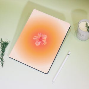 May include: A white and orange iPad case with a pink hibiscus flower design. The case has a subtle gradient effect from white to orange.