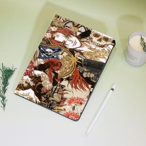 May include: A tablet case featuring a collage of pirate-themed illustrations in shades of brown, red, and white. The design includes a skull, pirate flag, compass, and character portraits. A white stylus and a lit candle are also visible.