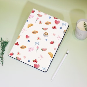 Könnte beinhalten: Weiße iPad-Hülle mit einem bunten Muster aus Früchten, Gebäck und Herzen. Das Muster enthält Erdbeeren, Wassermelonen, Papayas, Croissants, Kaffeetassen und Herzen.
