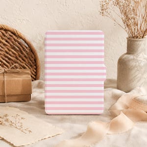 May include: A rectangular e-reader case featuring a repeating pattern of horizontal light pink and white stripes. The case has a smooth, flat surface with a small tab extending from the right side, designed to fit a standard electronic reading device.