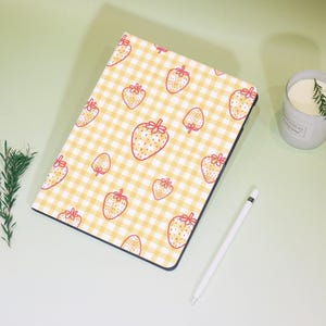 May include: A yellow and white gingham pattern iPad case with red strawberry illustrations.