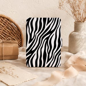Op de afbeelding: Een rechthoekige e-reader hoes met een contrastrijk zwart-wit zebrapatroon. De hoes heeft een glad, plat oppervlak met een verticale oriëntatie en een klein lipje aan de rechterkant om het beschermende apparaat te openen.