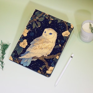 May include: A tablet case with an illustration of a white owl with blue eyes on a branch. The background is a dark blue night sky with yellow flowers and stars. A white stylus is next to the case.