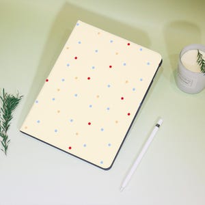 May include: A cream-colored notebook cover with a pattern of red, blue, and yellow dots. The cover has a black border.