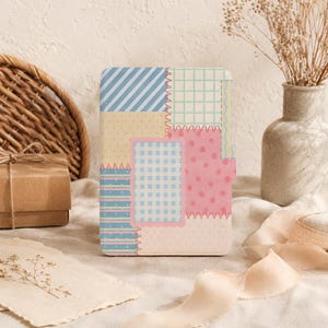 May include: A rectangular e-reader case featuring a patchwork design with various patterns including blue diagonal stripes, a green grid, yellow dots, blue gingham, and pink polka dots, all joined by decorative zigzag stitching.