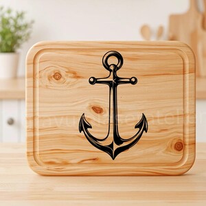 Puede incluir: Una tabla de cortar de madera con un dise&ntilde;o de ancla negra. La tabla tiene una veta de madera natural y un borde ligeramente redondeado.