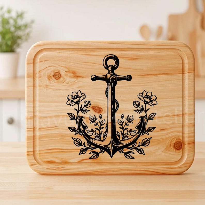 Puede incluir: Una tabla de cortar de madera con un ancla negra y un dise&ntilde;o floral. El ancla est&aacute; rodeada de hojas y flores.