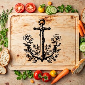 Puede incluir: Una tabla de cortar de madera con un dise&ntilde;o de ancla negra rodeada de detalles florales. El ancla tiene un dise&ntilde;o de cuerda y las flores son estilizadas.