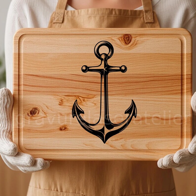 Puede incluir: Una tabla de cortar de madera con un dise&ntilde;o de ancla negra. La tabla tiene una veta de madera natural y un borde redondeado.