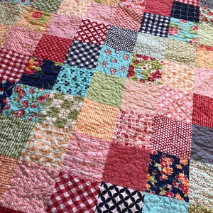 May include: A patchwork quilt with a variety of colorful squares, including red, blue, green, pink, and orange. The squares are arranged in a diagonal pattern, creating a visually interesting design.